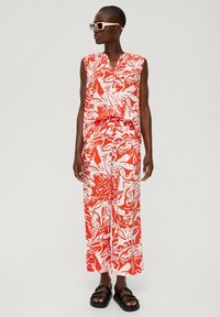 Beżowy komplet z bezrękawną bluzką i szerokimi spodniami w białym kolorze z wyraźnym czerwonym wzorem kwiatowym. Ubranie ma dekolt w kształcie litery V oraz elastyczny pas.