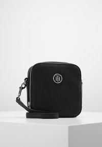 Borsa a tracolla nera realizzata in materiale texture con un accento del logo in argento, dotata di chiusura con zip e tracolla rimovibile.