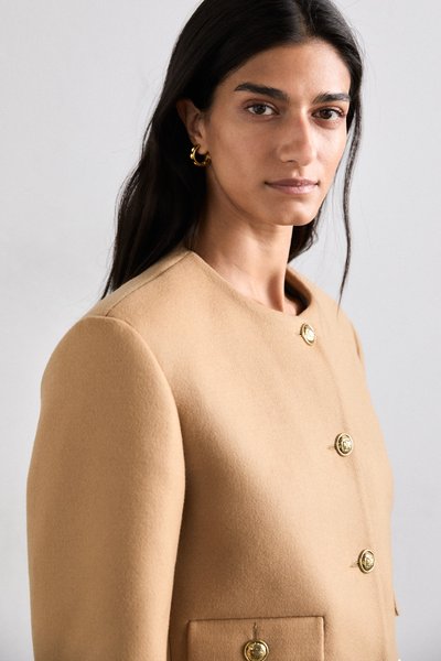 Manteau en mélange de laine couleur camel avec un col haut, un design croisé, des boutons dorés et des poches latérales. Texture lisse.