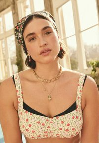 Floral-printed bustier top features red cherries and pink flowers on a cream background. Black accents on the neckline. Chunky gold jewelry.