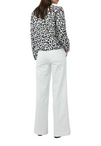 Bluse im Leopardenmuster in Schwarz und Weiß, kombiniert mit weißen weit geschnittenen Hosen. Das Outfit hat lange Ärmel und eine lockere Passform.
