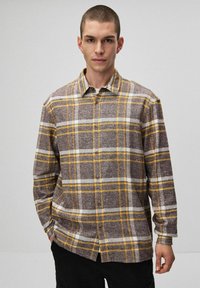 Brązowa i żółta koszula flanelowa w kratę z zapięciem na guziki, kołnierzykiem i długimi rękawami. Miękka tekstura z białymi akcentami w wzorze.