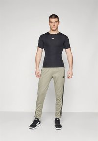 Camiseta preta justa de manga curta com logótipo branco, combinada com calças afuniladas verde-claro com riscas laterais pretas, usada com sapatilhas pretas de desporto.