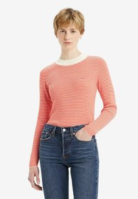 Langärmliges Oberteil mit rot-weißen Streifen und einem kremfarbigen gerippten Kragen, kombiniert mit dunkelblauen hochgeschnittenen Jeans.