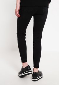 Jeans skinny negros con una textura suave, que presentan un clásico diseño de cinco bolsillos y dobladillo deshilachado. Llevados con zapatos de plataforma negros.