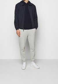 Námořnická bomberská bunda přes tmavý svetr s kapucí, v kombinaci se světlými šedými tepláky a bílými teniskami. Lehká tkanina a uvolněný střih po celou dobu.