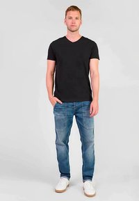 T-shirt nera con scollo a V abbinata a jeans di denim azzurro chiaro. I jeans presentano un classico design a cinque tasche e lievi dettagli effetto usurato. Scarpe da ginnastica bianche.