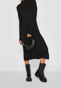 Robe noire côtelée à manches longues associée à des bottines noires brillantes à semelle épaisse, lacets, et un sac structuré noir.