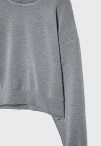 Sweatshirt gris clair à manches longues avec col rond, ourlet côtelé et panneau arrière légèrement plus long.