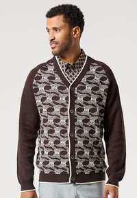 Hnědý kardigan s bílým geometrickým vzorem, s výstřihem do V, zapínáním na knoflíky a kontrastními okraji. Měkká pletená textura.