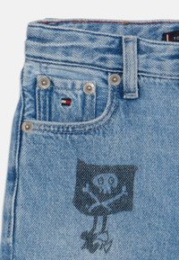 Shorts in denim azzurro chiaro con grafica di un teschio e ossa incrociate, dettagli in argento e una piccola etichetta con logo nei colori rosso, bianco e blu.