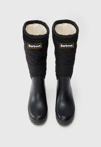 Bottes noires imperméables avec une tige en tissu matelassé et doublure en polaire, arborant le logo Barbour sur les côtés extérieurs. Design de bout arrondi lisse.