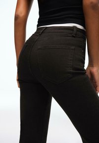 Jeans neri aderenti con una texture liscia, cinque tasche e cuciture a contrasto. Girovita visibile nella parte superiore con una leggera elasticità.