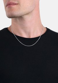 Collana in argento con piccoli anelli rotondi, indossata sopra una camicia nera aderente. La catena appare leggera e delicata sulla pelle.