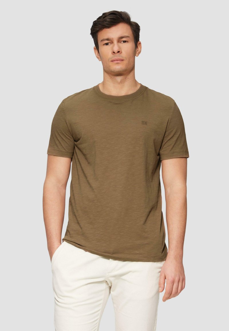 T-shirt vert olive à manches courtes avec un col rond et un logo subtil sur la poitrine. Tissu doux et texturé avec une coupe décontractée.