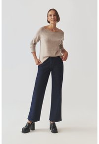 Beige Strickpullover mit einem Rundhalsausschnitt und drei Viertelärmeln, kombiniert mit dunkelblauen weiten Jeans und schwarzen Plateauslaufschuhen.