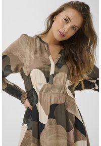 Ilga rankovėmis suknelė žemiškų tonalumų su mišriu raštu, apvaliu apykakle, susiaučiamu liemeniu ir struktūruotomis rankovėmis. Minkšta medžiaga.