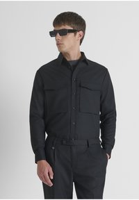 Zwarte button-up shirt met twee frontzakken, gemaakt van gladde stof. Draag het met zwarte broeken, voorzien van een riem met een sluiting.