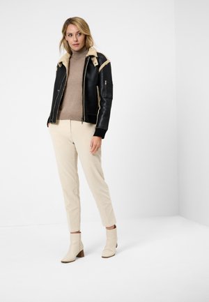 Zwarte leren bomberjack met schapenwol kraag, beige coltrui, beige broek en crèmekleurige enkellaarsjes met blokhak.
