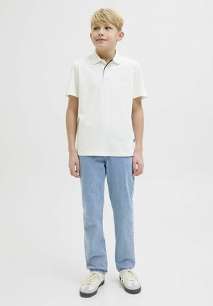 Chemise polo blanche avec un col, manches courtes et un petit emblème. Associations avec un jean bleu clair et des baskets grises.