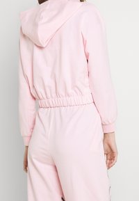 Felpa con cappuccio rosa con vita e polsini elasticizzati, caratterizzata da un tessuto a trama. Il retro presenta un design semplice senza ulteriori dettagli.