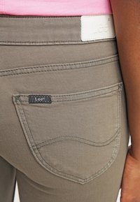 Jeans w kolorze oliwkowozielonym z tylną kieszenią z delikatnym przeszyciem oraz czarną metką "Lee". Teksturowana tkanina z solidnym pasem w talii.