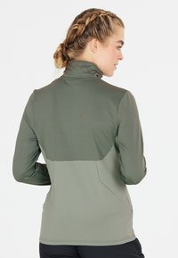 Olivegrünes Langarmshirt mit einem hohen Kragen und strukturiertem Stoff. Verfügt über ein kontrastierendes Panel auf der Rückseite und eine taillierte Silhouette.