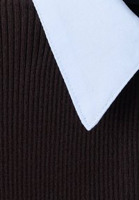Col triangulaire blanc sur un fond en tissu côtelé noir, montrant le détail des coutures le long du bord du col.