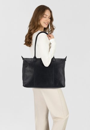Zwarte leren tote bag met dubbele handvatten, voorzien van een gestructureerde afwerking en een ritsluiting. Accenten zijn onder andere zichtbare stiksels en metalen hardware.