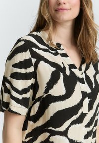 Blusa a maniche corte nera e beige con motivo a strisce zebrate, caratterizzata da un collo a V e un tessuto liscio e leggero.