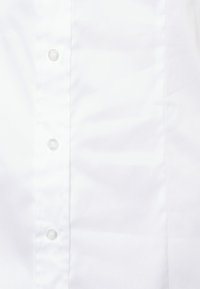 Chemise blanche à boutons, avec une texture lisse, dotée de boutons en plastique transparent et d'un col. Design simple et classique.