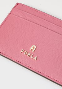 Rozā ādas karšu turētājs ar strukturētu virsmu, ar vairākiem nodalījumiem un zelta "Furla" logotipu priekšpusē. Malas ir kārtīgi izšūtas.