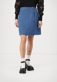 Denimskjørt, blått, med en svak A-linjeform og et liv. Brukt med svarte klumpete sko og hvite sokker. Teksturert svart topp med gjennomsiktige ermer.