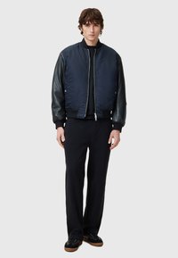 Navy bomber jacket with a satin body and leather sleeves, featuring a zip closure and ribbed cuffs, paired with black pants and shoes.