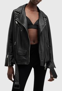 Black leather biker jacket with silver studs on shoulders, asymmetrical front zipper, side pockets, and adjustable belt buckle detail.