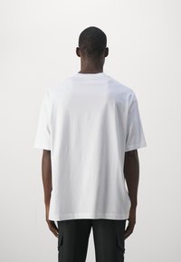 Bílý bavlněný tričko s uvolněným střihem, kulatým výstřihem a krátkými rukávy. Hladká textura, jednoduchý design a žádné viditelné logo nebo vzory.