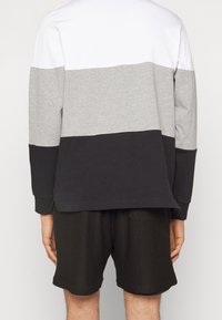 Långärmad top med färgblockering som har vita, grå och svarta sektioner, tillverkad av bomullsblandning, parat med svarta meshshorts.