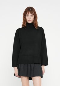 Svart turtleneck genser med ribbet søm og mansjetter, kombinert med en plisserte mørk grå skjørt. Myk tekstur; avslappet, oversized passform.