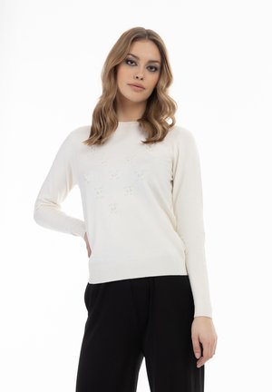 Pulover tricotat de culoare crem, cu manșoni lungi, decolteu rotund și detalii texturate cu perle mici aranjate într-un model pe față.
