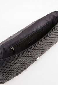 Borsa nera con un motivo esagonale testurizzato, dotata di un compartimento con zip e un rivestimento interno liscio. Accenti in hardware argentato.