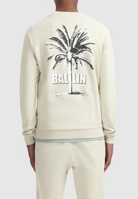 Licht beige sweatshirt met ribbels aan de boorden en onderrand, met een zwarte palmboom graphic en de tekst "BALLIN" op de achterkant. Soepele textuur.