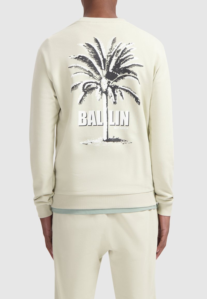 Licht beige sweatshirt met ribbels aan de boorden en onderrand, met een zwarte palmboom graphic en de tekst "BALLIN" op de achterkant. Soepele textuur.