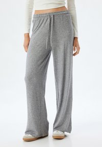 Graue, weite Sweatpants aus einem weichen Material, mit elastischem Bund, verstellbarem Kordelzug und Seitentaschen, ergänzt durch leichte Schuhe.