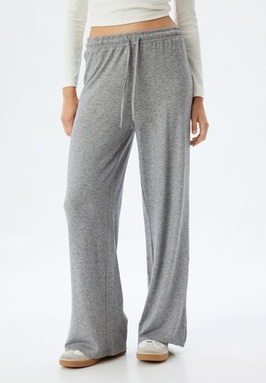 Grijze, wijde-snij sweatpants met een zachte textuur, elastische tailleband, verstelbaar trekkoord en zijzakken, aangevuld met lichte schoenen.