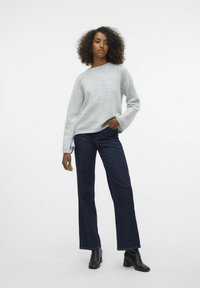 Pullover grigio chiaro con maniche lunghe, abbinato a jeans a gamba larga blu scuro e stivaletti neri con tacco. Texture liscia e vestibilità casual.