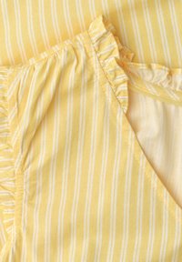 Tissu rayé jaune et blanc avec bords froncés, montrant les coutures et un coin plié révélant l'envers du textile.