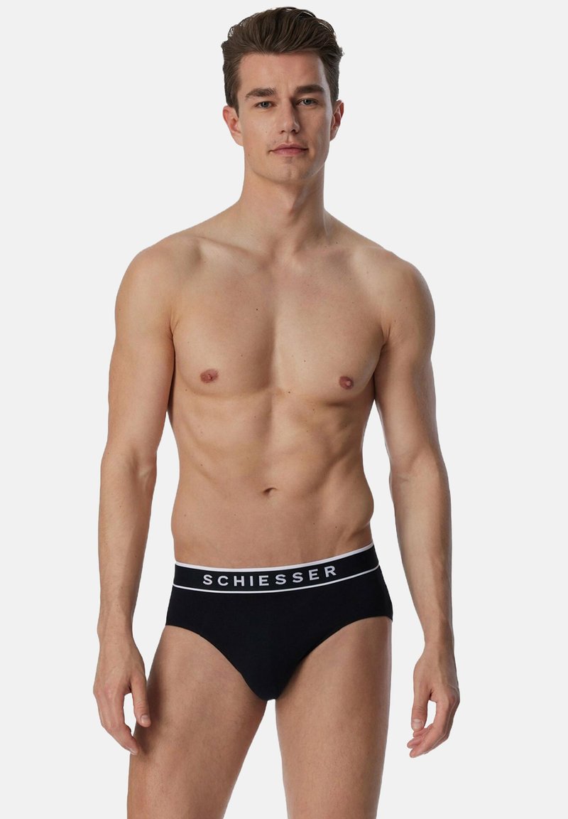 Zwarte katoenen slips met een witte merkband. De slips hebben een klassiek, snug fit en een gladde textuur. Het model staat rechtop.