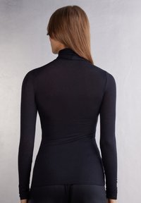 Zwart langemouwen top met hoge hals en aangesloten ontwerp, gemaakt van gladde, rekbare stof, met een naadloze achterkant en slanke uitstraling.