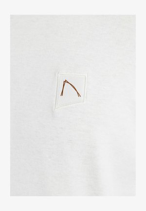 Biely bavlnený tričko s malou, štvorcovou nášivkou s hnedým geometrickým dizajnom. Hladká textúra s minimálnymDetailing.