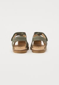 Grønne lær sandaler med åben design, justerbare stropper og tan indersål. Har flad hæl og synlægning langs kanterne.
